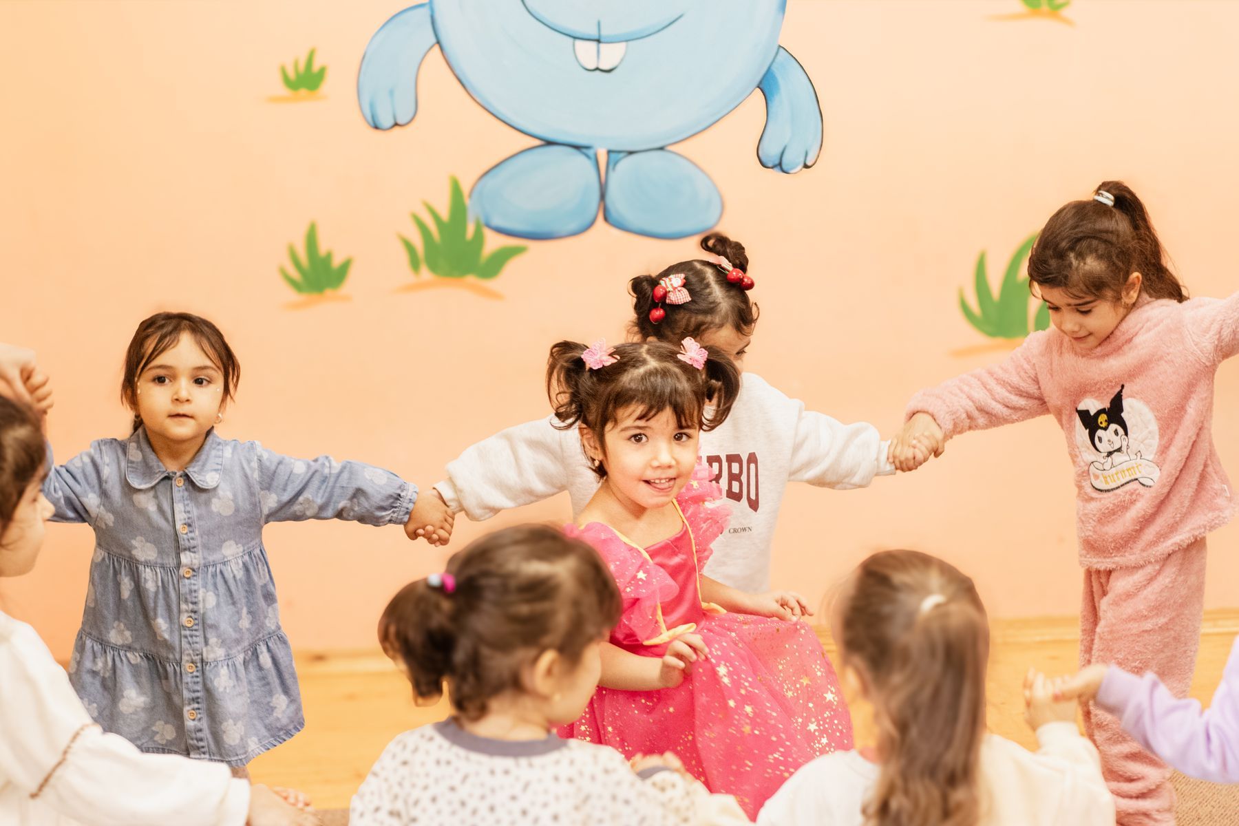 Sınıfta el ele tutuşup çember oyunu oynayan anaokulu çocukları